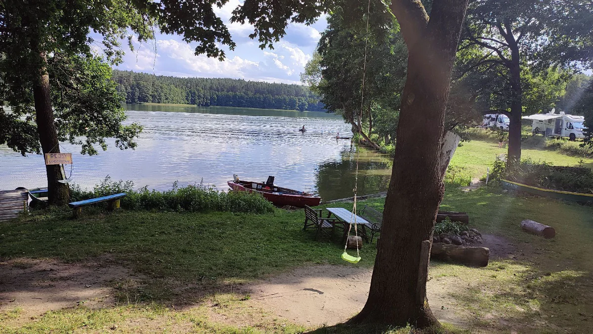 Grünes Seeufer des Campingplatzes mit Boot, Steg und Sitzplätzen
